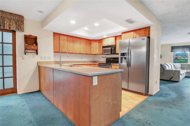 kitchen featuring kitchen peninsula, light carpet, appliances with stainless steel finishes, and a tray ceiling