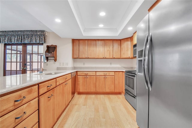 kitchen with sink, french doors, stainless steel appliances, a raised ceiling, and light wood-type flooring