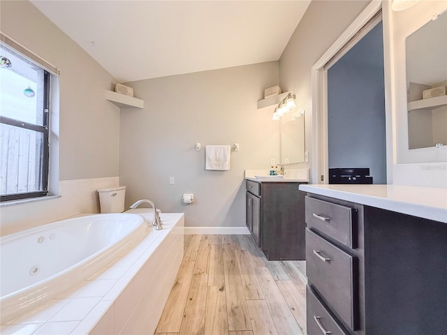 bathroom featuring hardwood / wood-style floors, vanity, toilet, and tiled bath