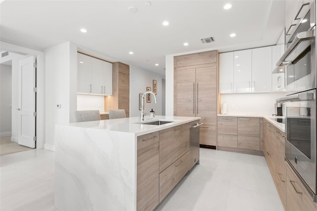 kitchen with stainless steel appliances, a spacious island, sink, light brown cabinets, and white cabinets