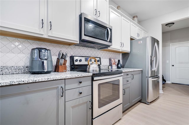 kitchen with appliances with stainless steel finishes, gray cabinets, tasteful backsplash, and white cabinetry