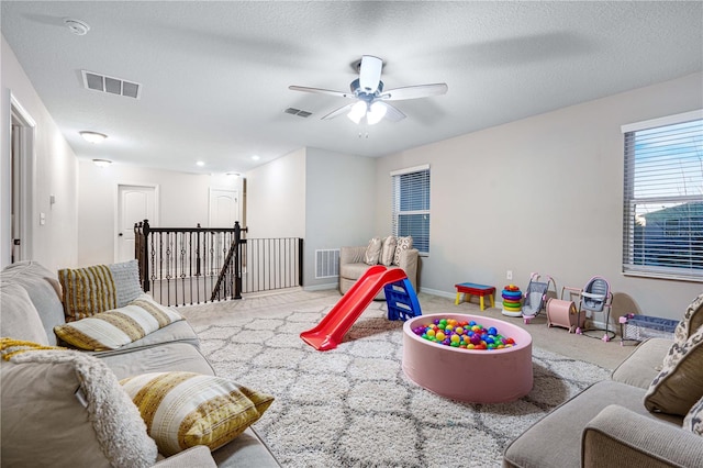 game room featuring light carpet, ceiling fan, and a textured ceiling