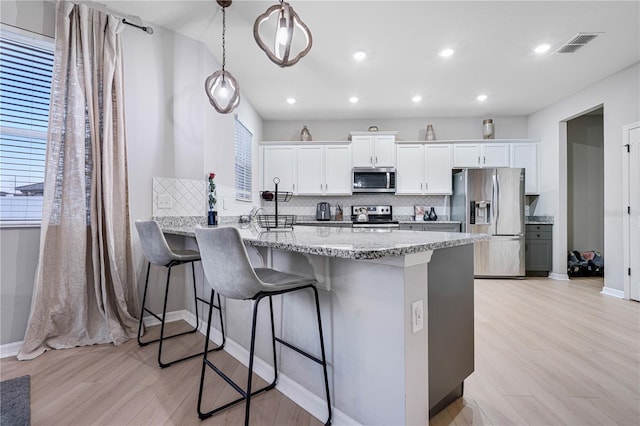 kitchen featuring pendant lighting, kitchen peninsula, light hardwood / wood-style floors, white cabinetry, and stainless steel appliances