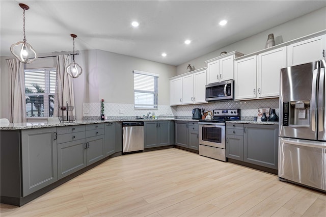 kitchen with gray cabinetry, hanging light fixtures, decorative backsplash, appliances with stainless steel finishes, and white cabinetry