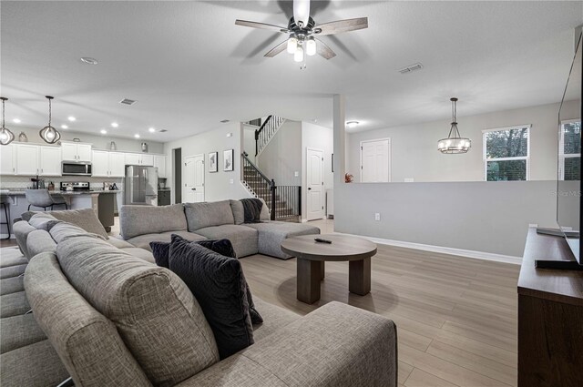 living room with ceiling fan with notable chandelier and light wood-type flooring