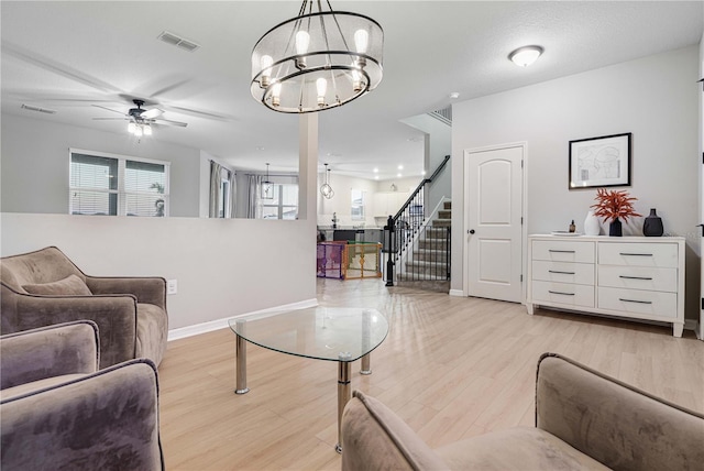 living room with ceiling fan with notable chandelier, light hardwood / wood-style floors, and a textured ceiling