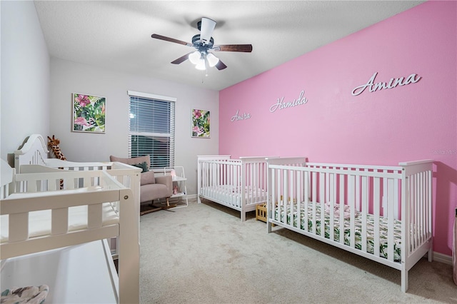 carpeted bedroom with ceiling fan and a nursery area