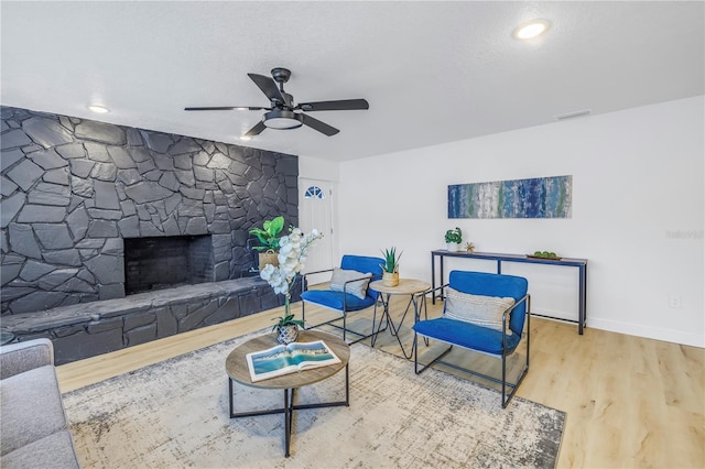 living room featuring hardwood / wood-style floors, a stone fireplace, a textured ceiling, and ceiling fan