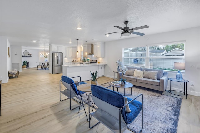 living room featuring ceiling fan with notable chandelier, light hardwood / wood-style flooring, and a textured ceiling