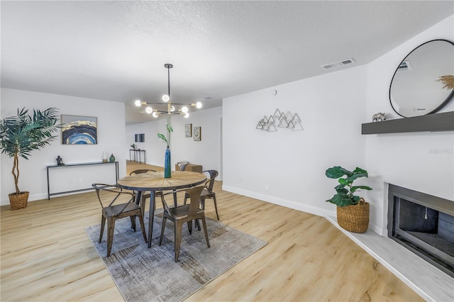 dining space with wood-type flooring, a notable chandelier, and a textured ceiling