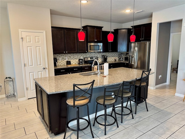 kitchen with decorative light fixtures, sink, a kitchen island with sink, stainless steel appliances, and light stone countertops