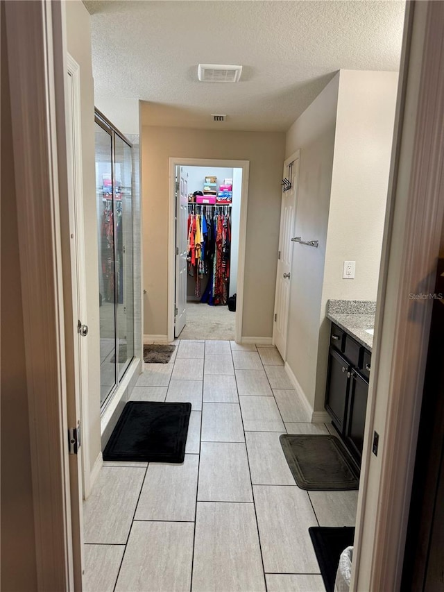 bathroom with an enclosed shower, vanity, tile patterned flooring, and a textured ceiling