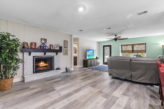 living room featuring a fireplace, light hardwood / wood-style floors, a textured ceiling, and ceiling fan