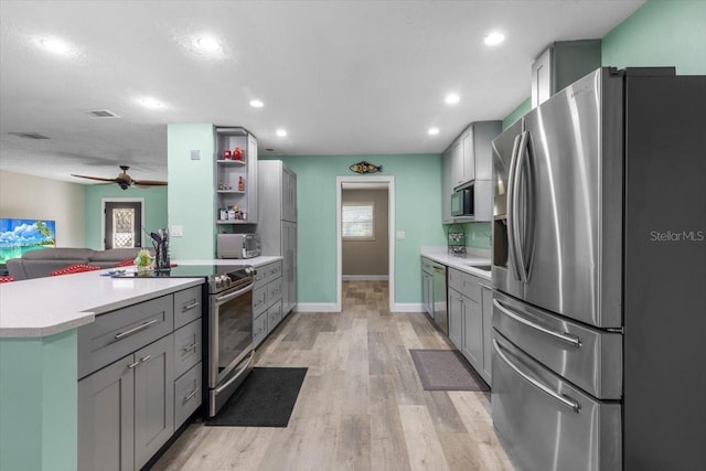 kitchen with gray cabinetry, ceiling fan, appliances with stainless steel finishes, and light hardwood / wood-style flooring