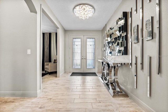 foyer featuring a textured ceiling, french doors, and a notable chandelier