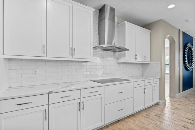 kitchen with white cabinetry, light hardwood / wood-style floors, black electric stovetop, wall chimney range hood, and light stone counters