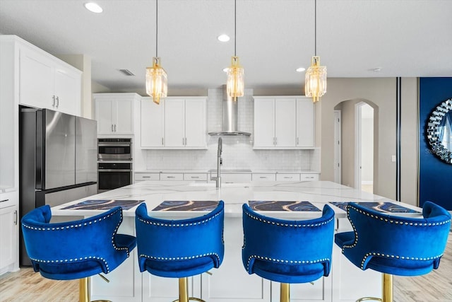 kitchen featuring decorative light fixtures, light stone countertops, wall chimney exhaust hood, and stainless steel appliances