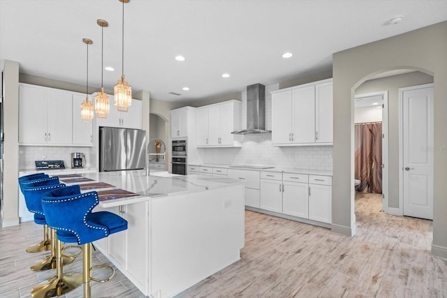 kitchen featuring white cabinets, appliances with stainless steel finishes, wall chimney exhaust hood, and an island with sink