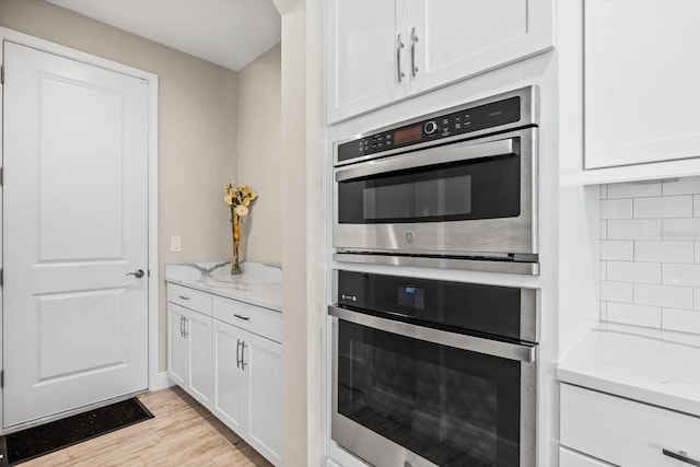 kitchen featuring white cabinetry, light stone counters, and stainless steel double oven