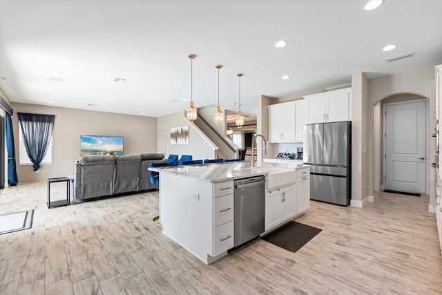 kitchen featuring stainless steel appliances, sink, white cabinets, and an island with sink