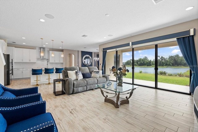 living room featuring light wood-type flooring, a textured ceiling, and a water view