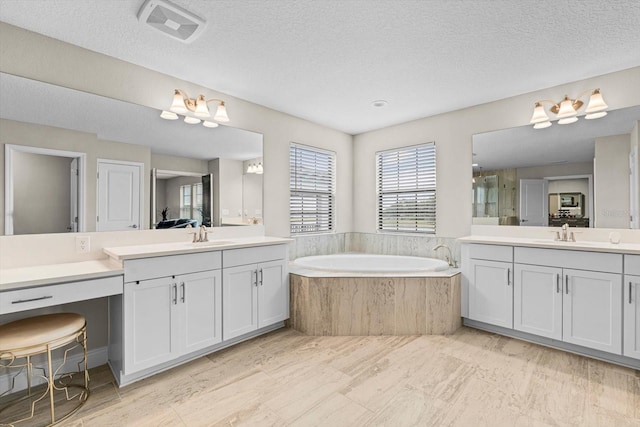 bathroom featuring a textured ceiling, tiled bath, and vanity