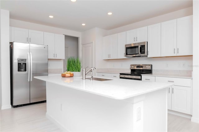 kitchen with appliances with stainless steel finishes, sink, white cabinets, and a kitchen island with sink