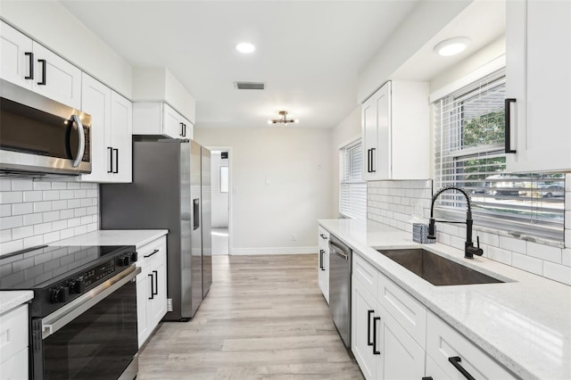 kitchen with light stone countertops, appliances with stainless steel finishes, light wood-type flooring, sink, and white cabinetry