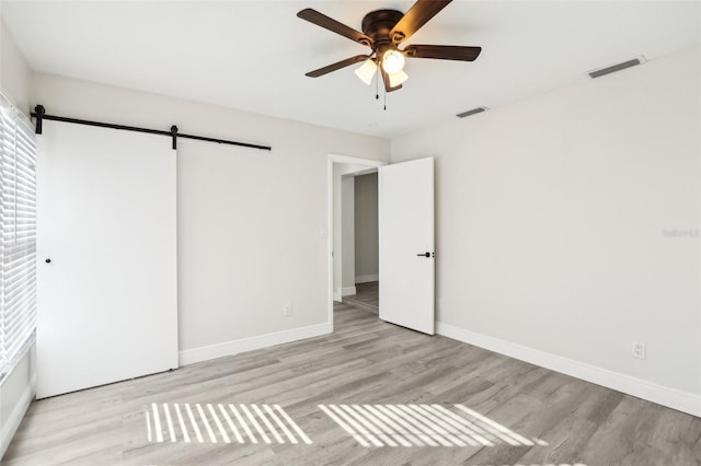 unfurnished bedroom featuring a barn door, light hardwood / wood-style floors, and ceiling fan