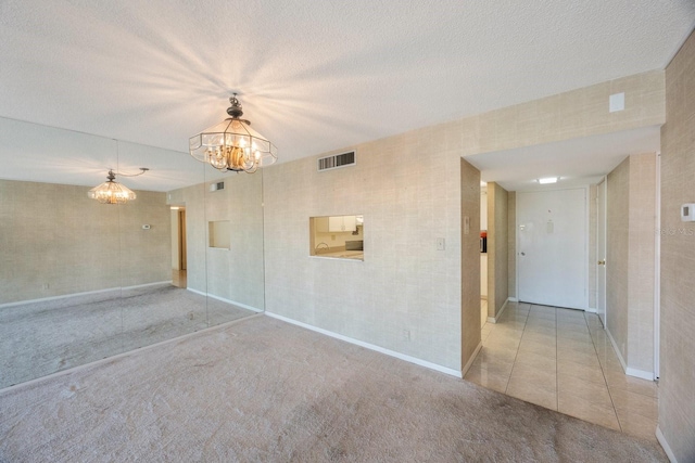 empty room with light colored carpet, a textured ceiling, and a chandelier