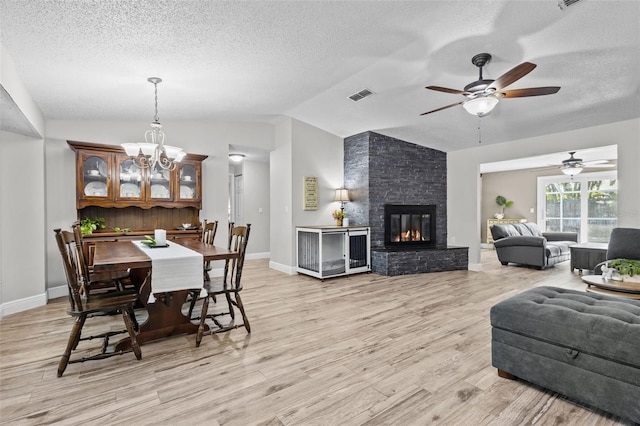 dining space with light wood-type flooring, vaulted ceiling, a stone fireplace, and ceiling fan with notable chandelier