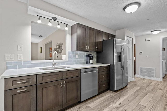 kitchen with sink, stainless steel appliances, light hardwood / wood-style floors, decorative backsplash, and dark brown cabinets