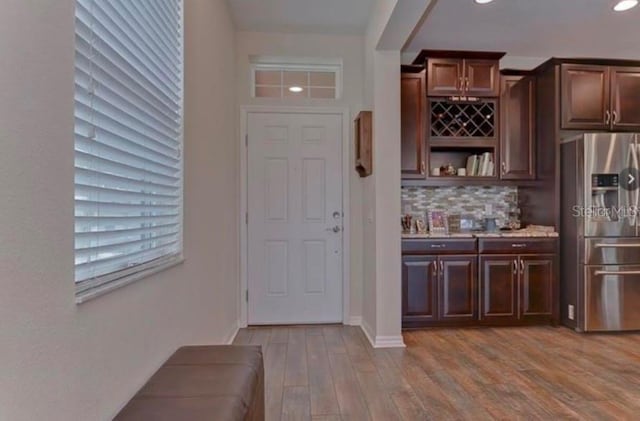 bar featuring stainless steel fridge, light wood-type flooring, dark brown cabinetry, and backsplash