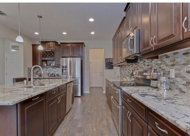 kitchen with pendant lighting, backsplash, sink, hardwood / wood-style flooring, and appliances with stainless steel finishes