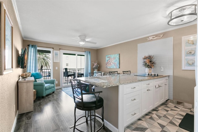 kitchen with light stone countertops, a kitchen bar, white cabinetry, and ornamental molding