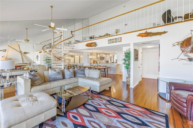 living room with ceiling fan, a towering ceiling, and wood-type flooring