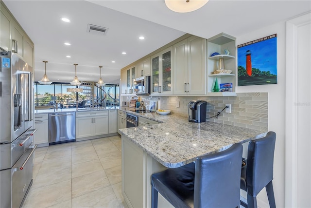 kitchen featuring stainless steel appliances, kitchen peninsula, a kitchen bar, light stone counters, and decorative light fixtures