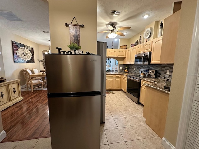 kitchen featuring stainless steel appliances, light tile patterned floors, decorative backsplash, and dark stone counters