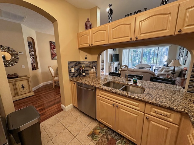 kitchen with sink, light brown cabinets, light tile patterned floors, stainless steel dishwasher, and dark stone counters