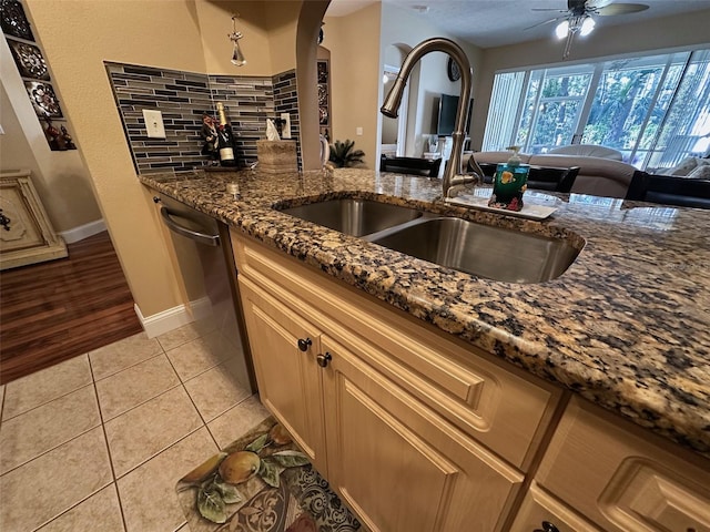 kitchen featuring light tile patterned flooring, dishwasher, sink, dark stone countertops, and ceiling fan