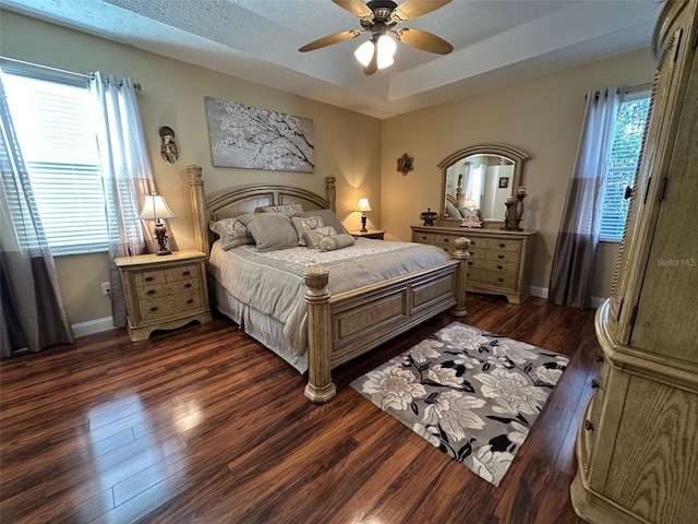 bedroom with a textured ceiling, dark wood-type flooring, a raised ceiling, and ceiling fan