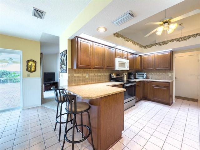 kitchen featuring stainless steel electric stove, a kitchen breakfast bar, backsplash, kitchen peninsula, and light tile patterned floors