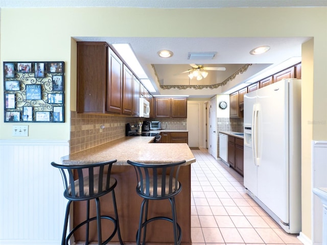 kitchen with ceiling fan, kitchen peninsula, a tray ceiling, white appliances, and a kitchen breakfast bar