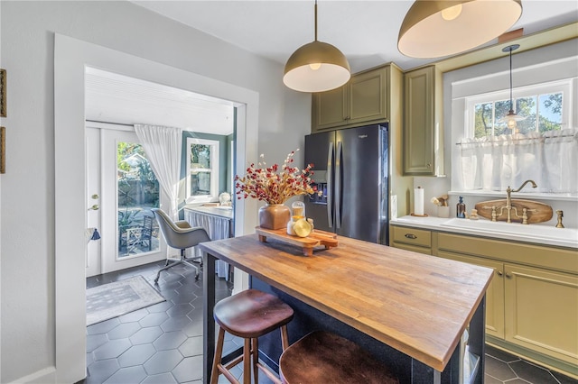 kitchen with stainless steel refrigerator with ice dispenser, hanging light fixtures, butcher block counters, and sink