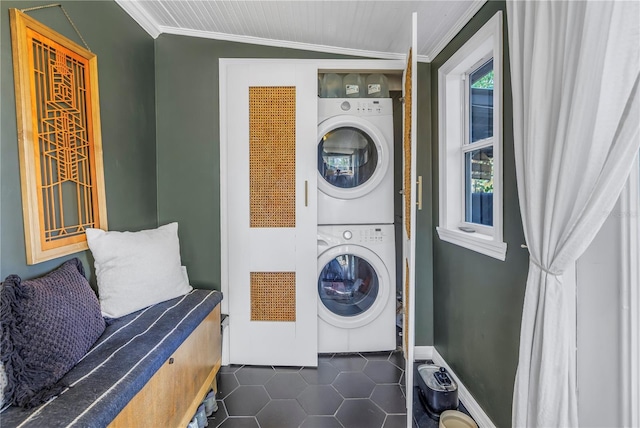 clothes washing area featuring dark tile patterned flooring, stacked washer / drying machine, and crown molding