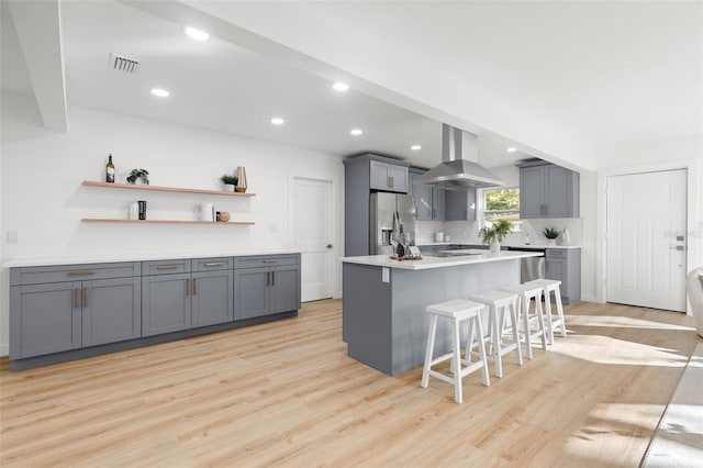 kitchen with gray cabinetry, ventilation hood, stainless steel fridge, a breakfast bar area, and light wood-type flooring