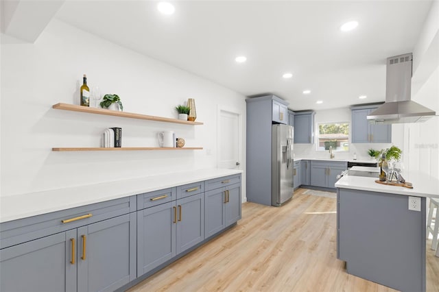 kitchen with sink, range hood, stainless steel refrigerator with ice dispenser, a kitchen island, and light wood-type flooring