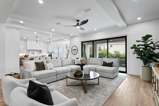 living room with beamed ceiling, ceiling fan, and light wood-type flooring