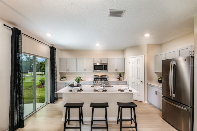 kitchen with light hardwood / wood-style flooring, stainless steel appliances, a breakfast bar area, and an island with sink