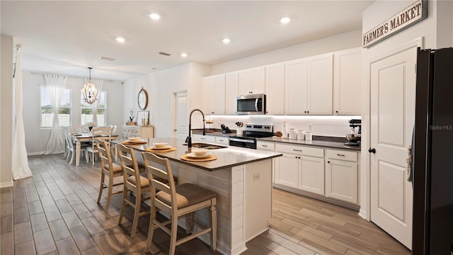 kitchen with a center island with sink, sink, appliances with stainless steel finishes, decorative light fixtures, and a breakfast bar area